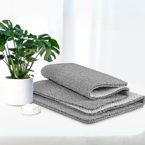 Gray mat rolled and folded in a stack, showing its white grid backing, beside a potted plant and a small soap dish. 2