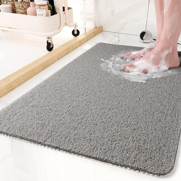 Gray loop-textured mat on a bathroom floor with a person's soapy bare feet standing on it, a rolling storage cart nearby. 1