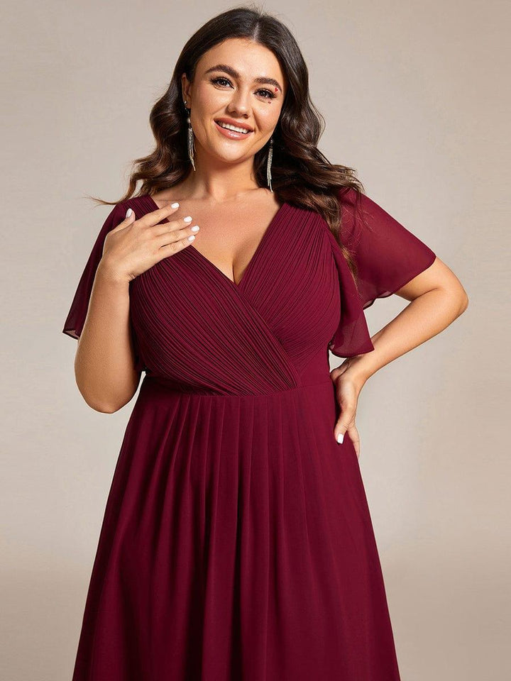 Close-up of the burgundy dress on a plus-size model, hand on chest, showing the pleated crossover bodice and flutter sleeves. 51