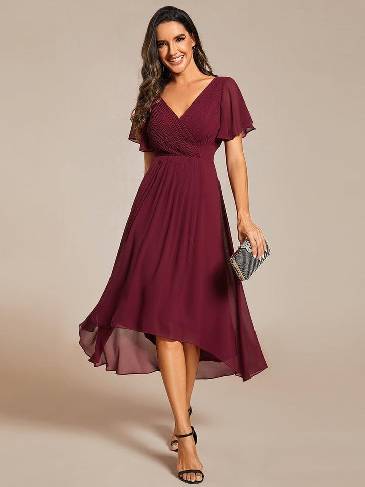 Burgundy version of the chiffon dress, front view, with pleated wrap bodice, flutter sleeves and a sparkly clutch. 3