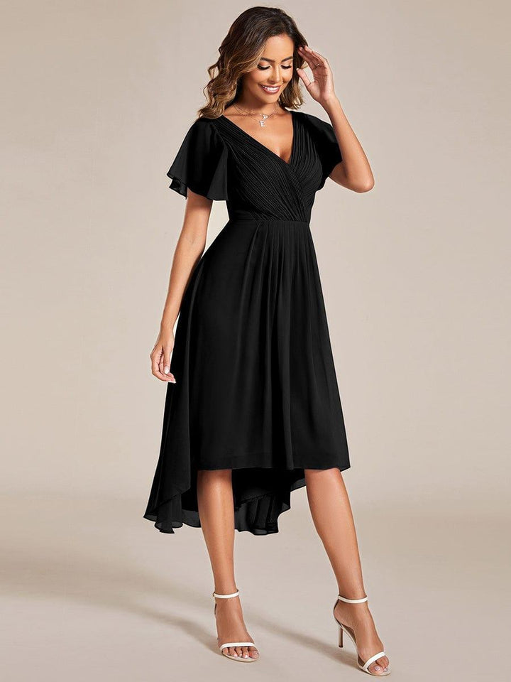 Three-quarter view of a smiling model in the black chiffon dress, touching her hair, showing the pleated waist and asymmetrical hem. 25