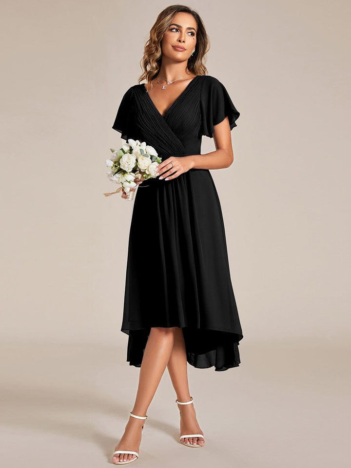 Model in the black dress holding a small bouquet of white roses, standing with crossed legs in white heeled sandals. 24