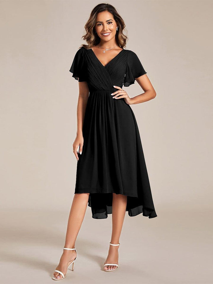 Model in a black pleated-bodice chiffon dress with flutter sleeves and a high-low hem, one hand on hip, with white heeled sandals. 21