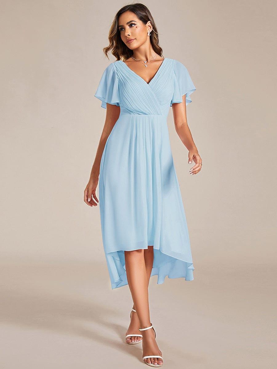Model in a light blue chiffon high-low dress with pleated V-neck, flutter sleeves and white strappy heels, walking toward the camera. 84