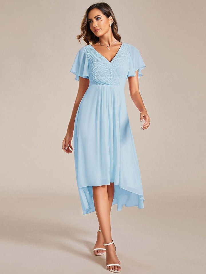 Model in a light blue chiffon high-low dress with pleated V-neck, flutter sleeves and white strappy heels, walking toward the camera. 84