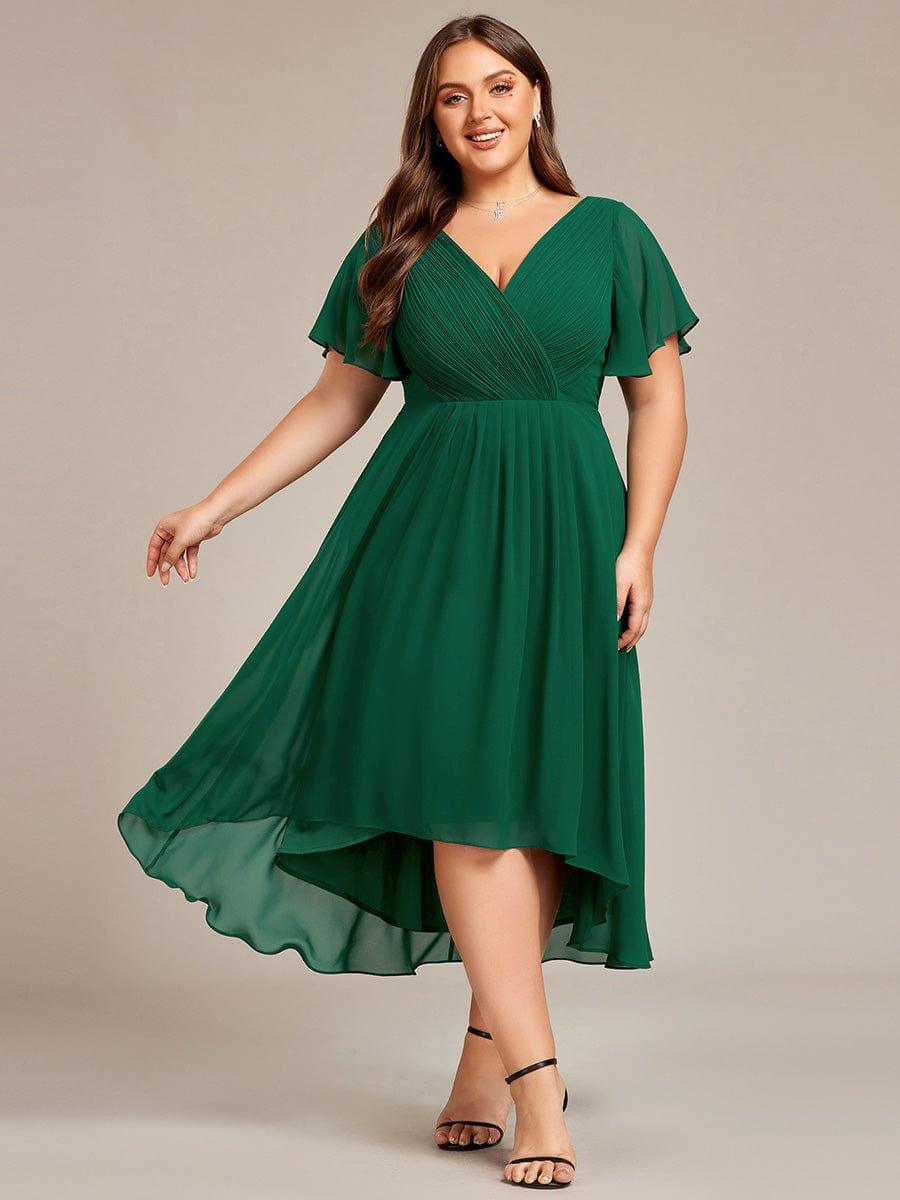 Plus-size model in the dark green version of the dress, skirt swinging out to show the sheer high-low hem, with black heels. 36