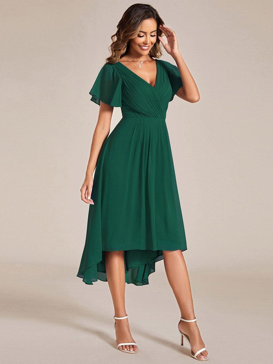 Dark green chiffon dress in a three-quarter pose, hand raised to her hair, showing the flowing skirt and hem. 14