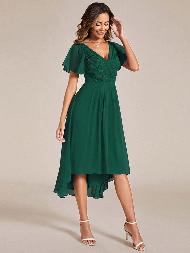 Dark green chiffon dress in a three-quarter pose, hand raised to her hair, showing the flowing skirt and hem. 14