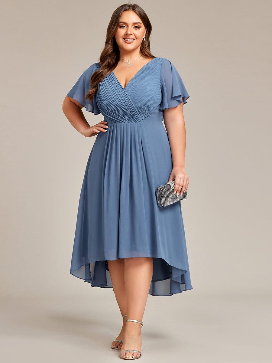 Plus-size model smiling in the dusty blue dress, one hand on hip, holding a black clutch and wearing silver heels. 44