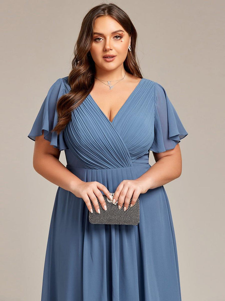 Close-up of the pleated wrap bodice and flutter sleeves in dusty blue, model holding a small black sparkly clutch. 43