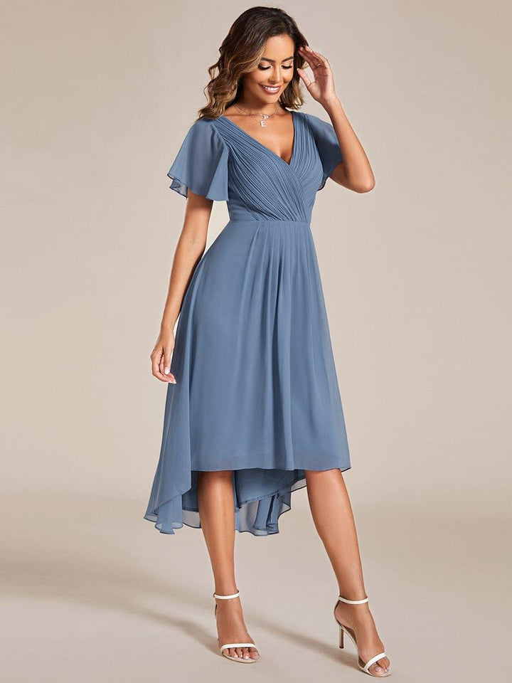 Three-quarter view of the dusty blue chiffon dress with the model touching her hair, showing the high-low hemline. 9