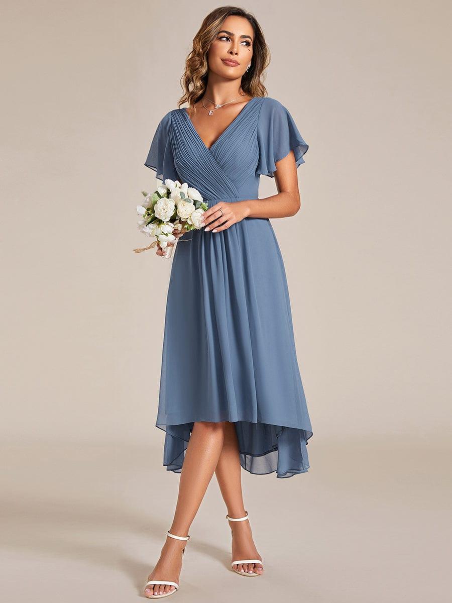 Model in the dusty blue high-low dress holding a small bouquet of white flowers, looking off to the side. 8