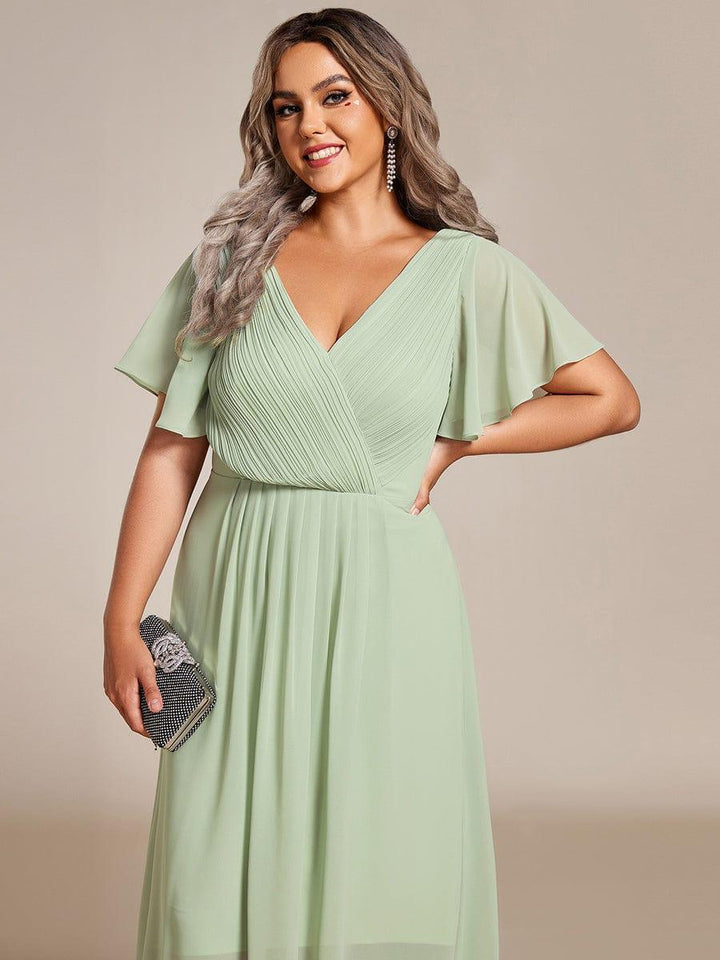 Close-up of the sage green dress's pleated V-neck bodice and flutter sleeves, worn by a smiling plus-size model holding a sparkly clutch. 83