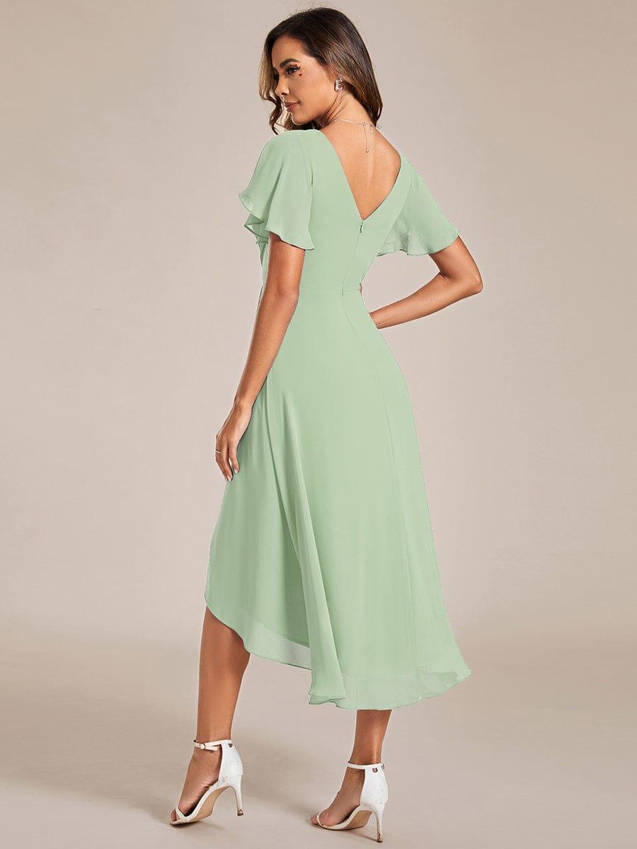 Back view of a model in the sage green chiffon dress, showing the V-back, zipper, flutter sleeves and asymmetrical hem. 77