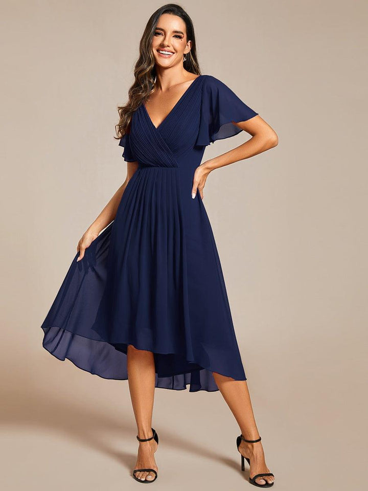 Model in the navy dress smiling, one hand on hip and the other lifting the sheer chiffon skirt to show the high-low hem. 54