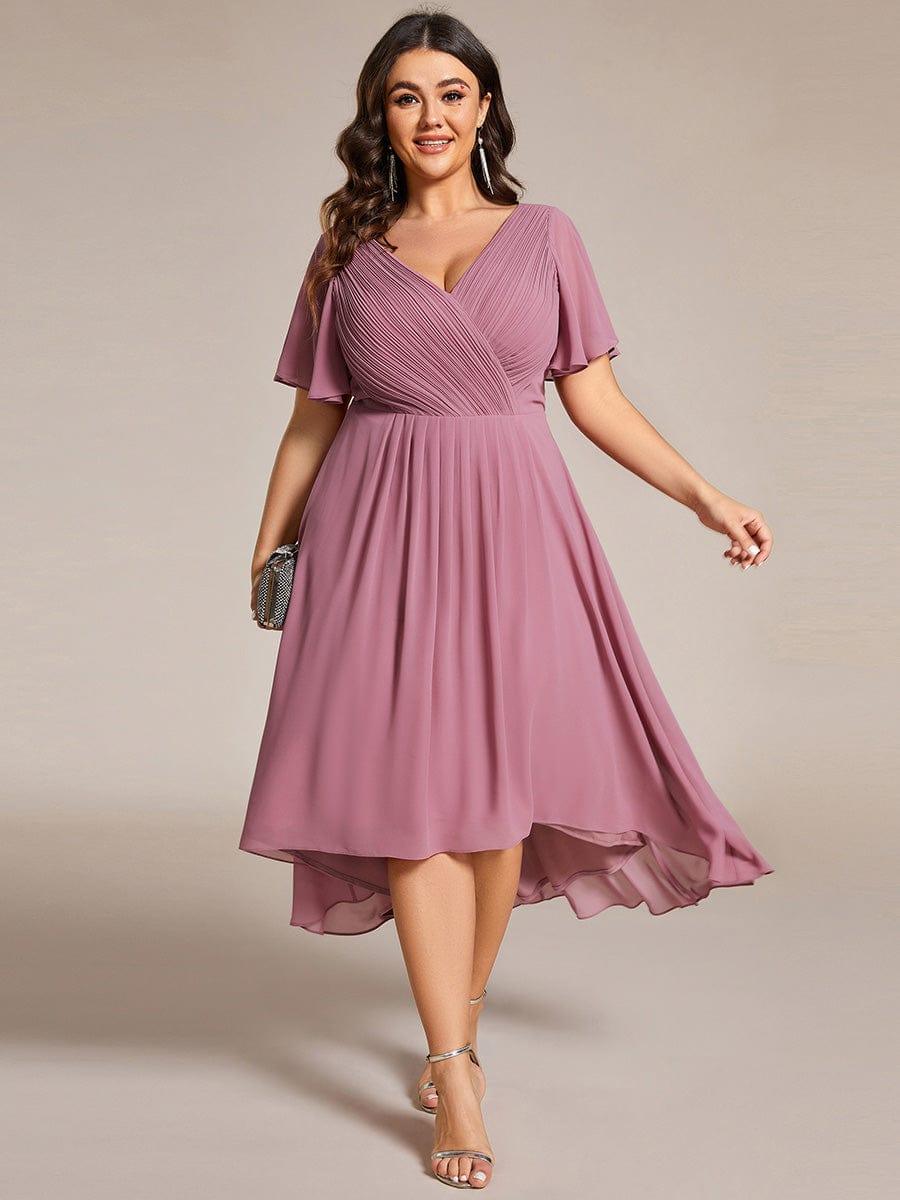 Plus-size model in the mauve pink high-low chiffon dress, front view, holding a small clutch and wearing gold sandals. 63