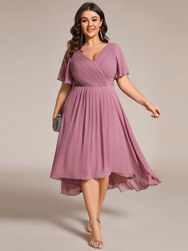 Plus-size model in the mauve pink high-low chiffon dress, front view, holding a small clutch and wearing gold sandals. 63