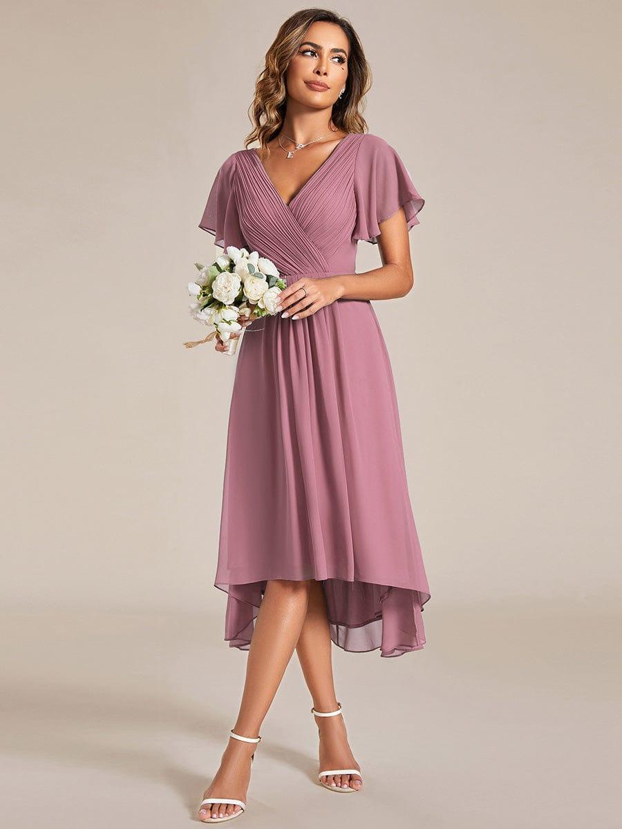 Model in the mauve pink chiffon dress holding a small bouquet of white flowers, glancing to the side in white heels. 60