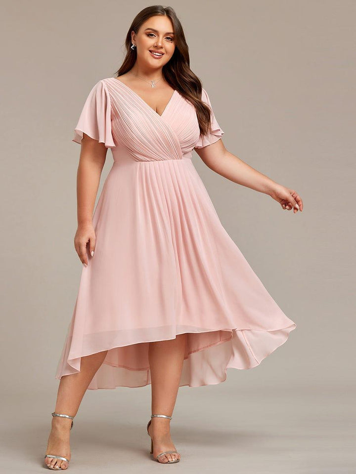 Plus-size model in the pink chiffon dress, smiling with one arm extended, showing the pleated skirt and high-low hem. 34