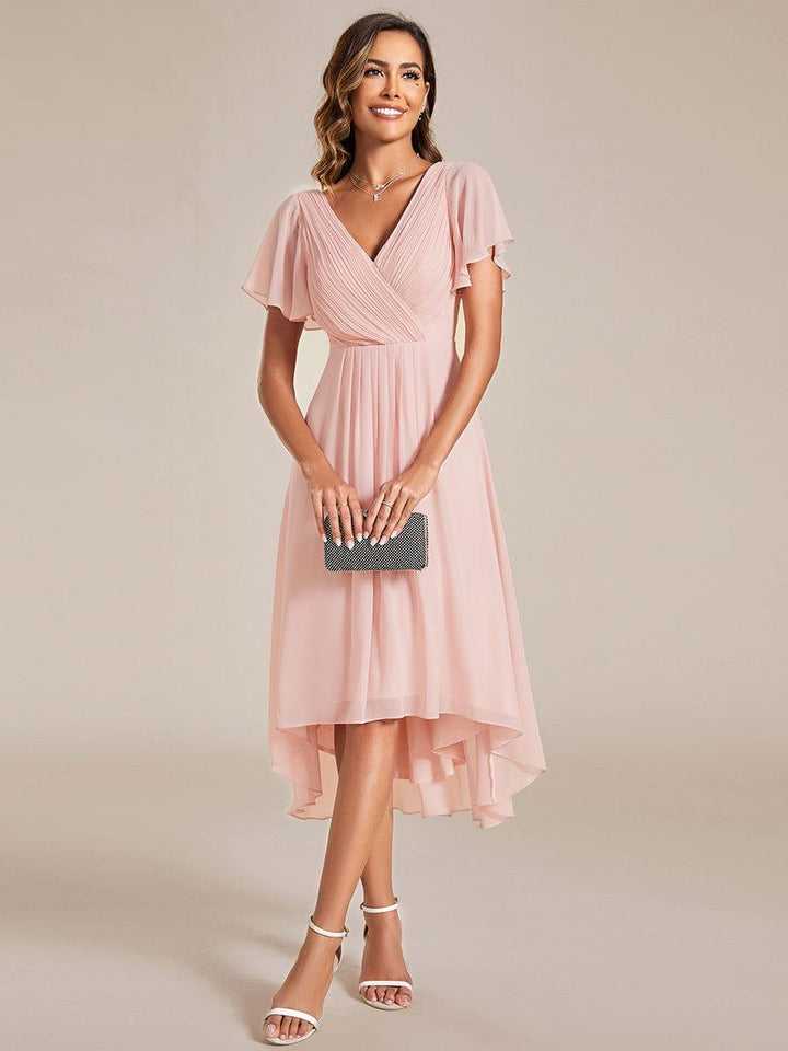 Pink chiffon dress, front view, with pleated wrap bodice and flutter sleeves, model holding a small black clutch. 15