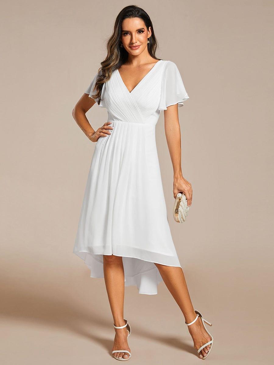 Model in the white chiffon dress standing with one hand on her hip and holding a pearl clutch, front view. 71