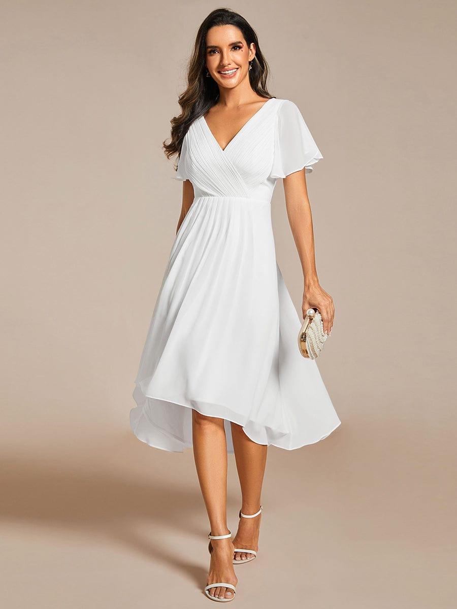 Model in the white high-low chiffon dress with pleated V-neck bodice, holding a small pearl-beaded clutch, front view. 68