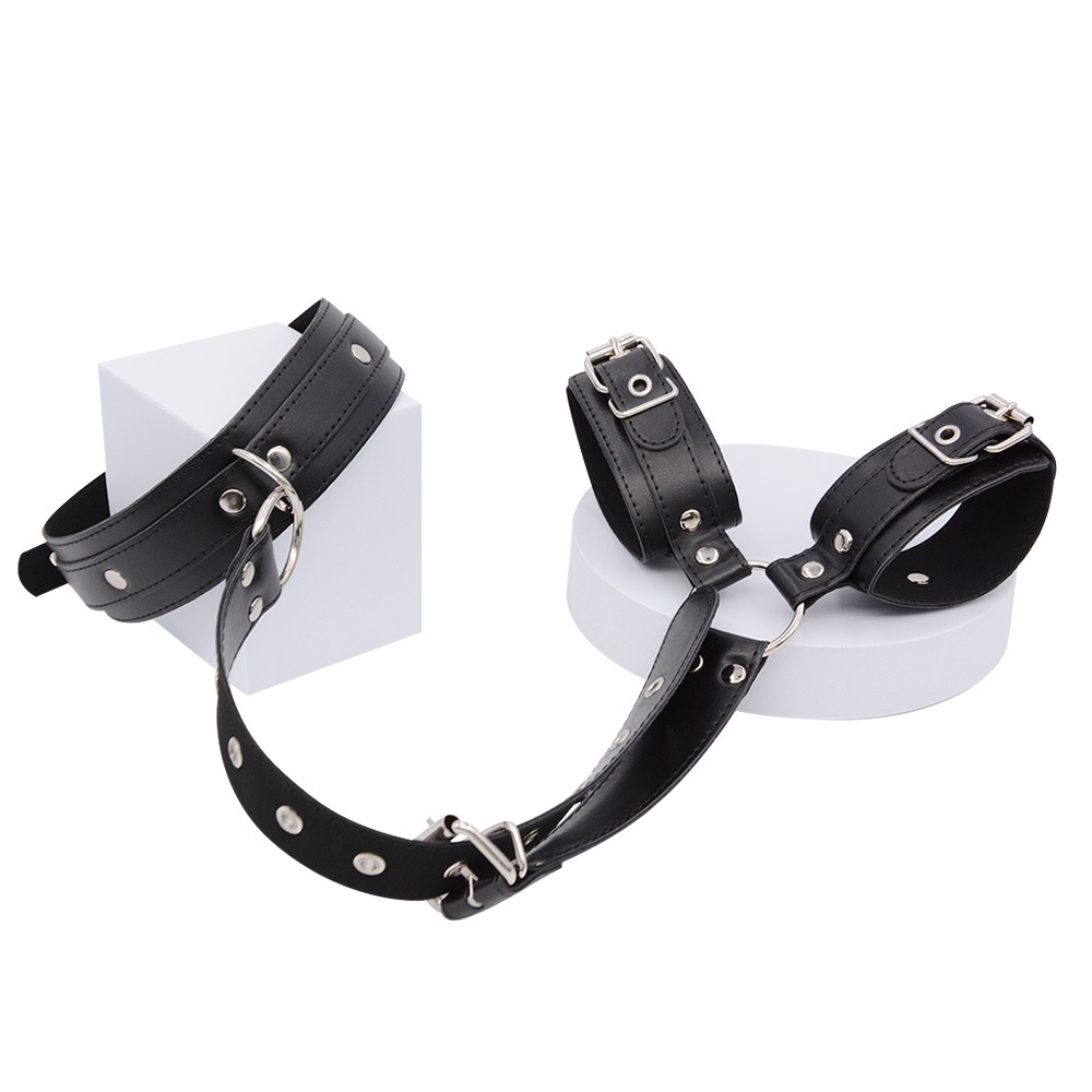Black collar and wrist cuffs displayed on white blocks and a round platform, joined by a studded strap with silver buckles. 16