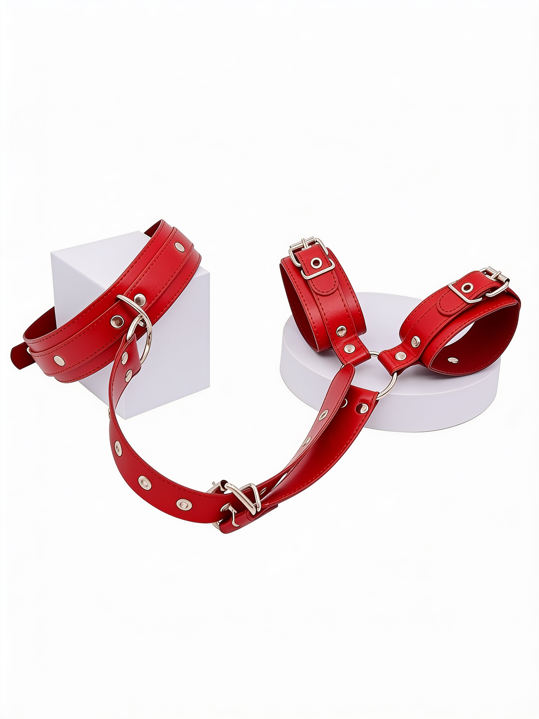 Red set displayed on white geometric blocks, with the collar on one block and the two cuffs on a round platform, linked by a strap. 12