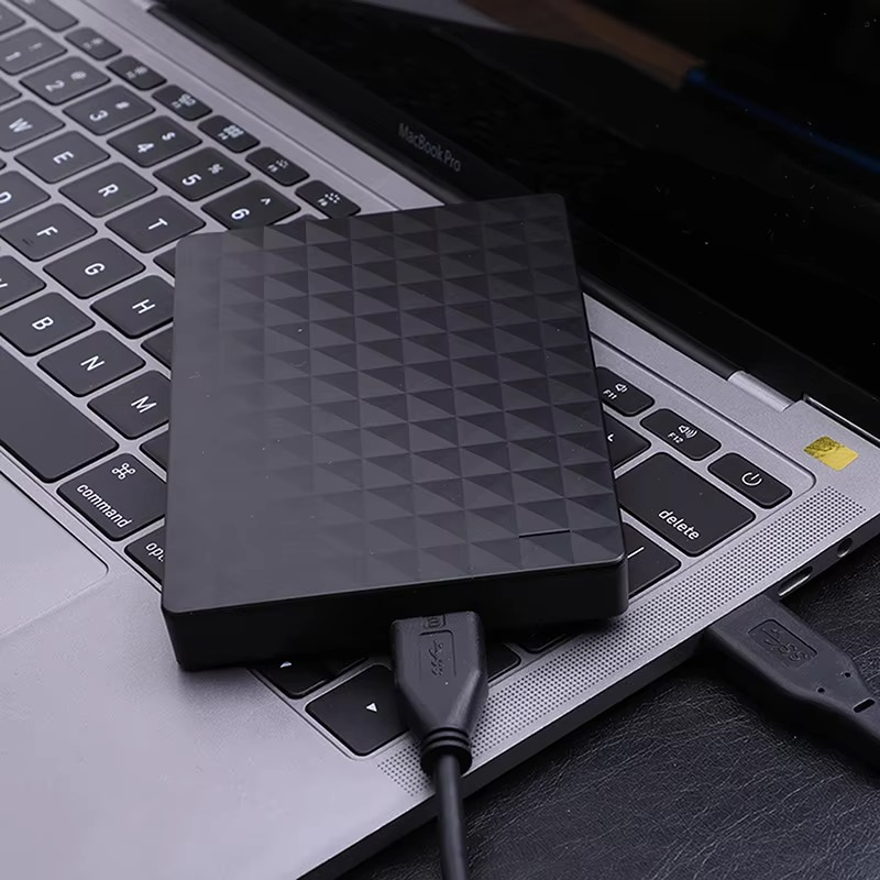 Black textured drive resting on a laptop keyboard with a USB cable plugged in, shown in use. 3