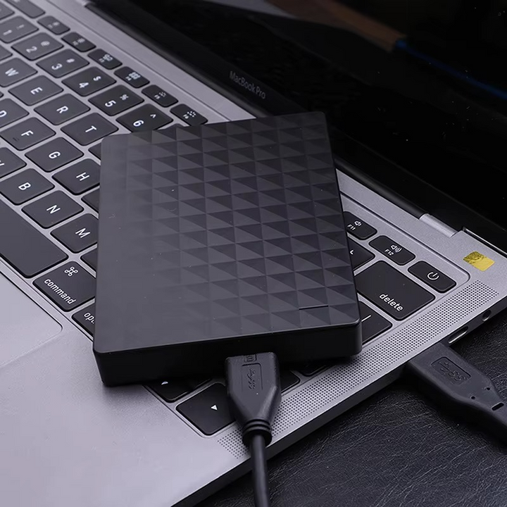 Black textured drive resting on a laptop keyboard with a USB cable plugged in, shown in use. 3