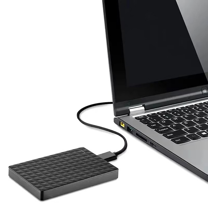 Drive sitting beside an open laptop, connected to its side USB port by a black cable. 4