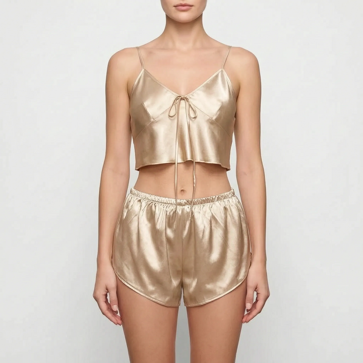 Model facing forward in the champagne satin camisole with looped front tie and shorts with curved hems, against a light gray backdrop. 6