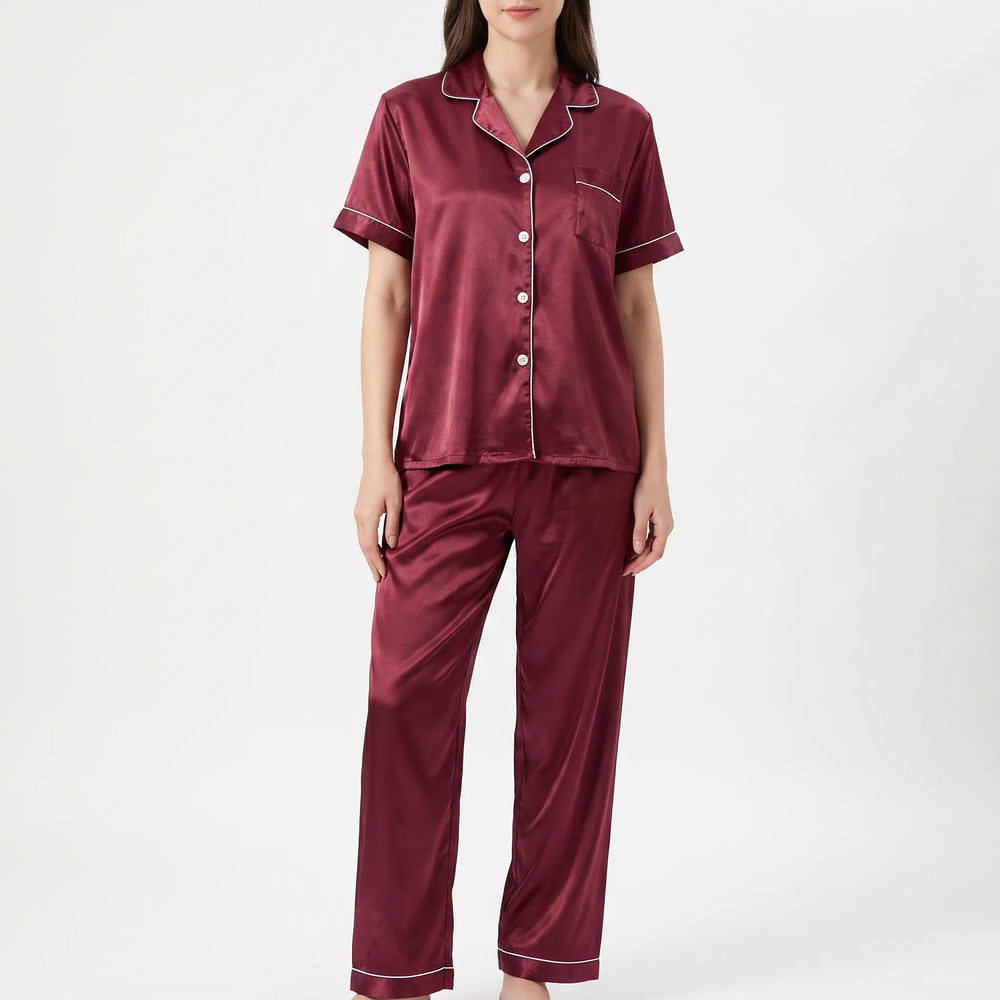 Front view of a woman wearing a burgundy satin pajama set with white piping, buttoned shirt, chest pocket and long pants. 2