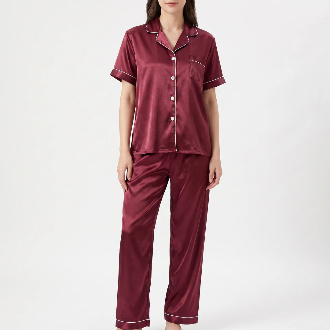 Front view of a woman wearing a burgundy satin pajama set with white piping, buttoned shirt, chest pocket and long pants. 2