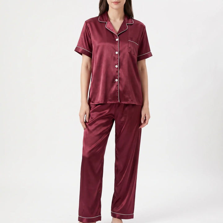 Front view of a woman wearing a burgundy satin pajama set with white piping, buttoned shirt, chest pocket and long pants. 2
