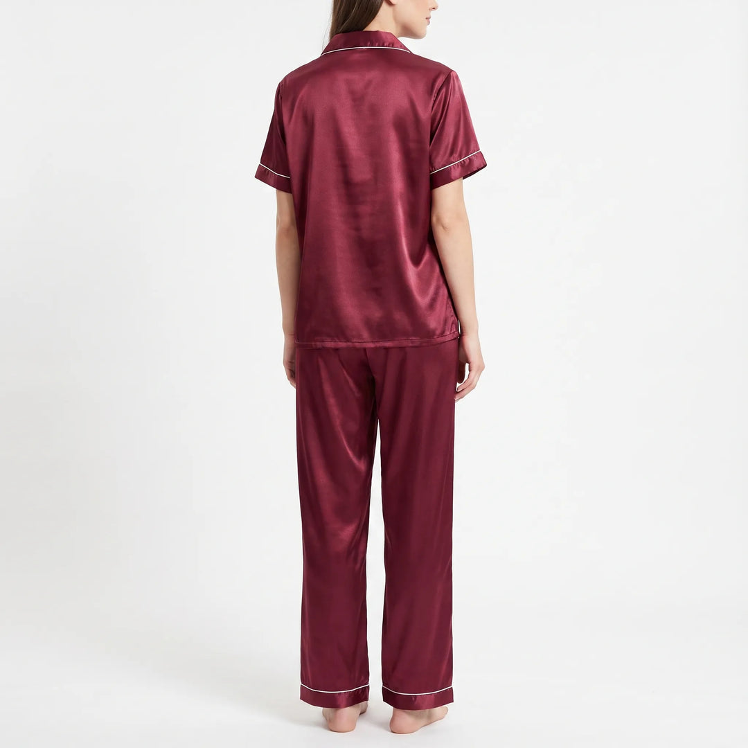 Back view of a woman in the burgundy satin pajama set, showing the plain shirt back and piped pants hems. 3