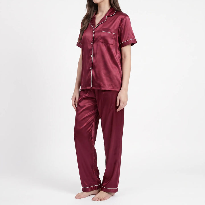 Three-quarter side view of a woman in the burgundy satin pajamas, showing the notched collar, piped pocket and straight-leg pants. 4