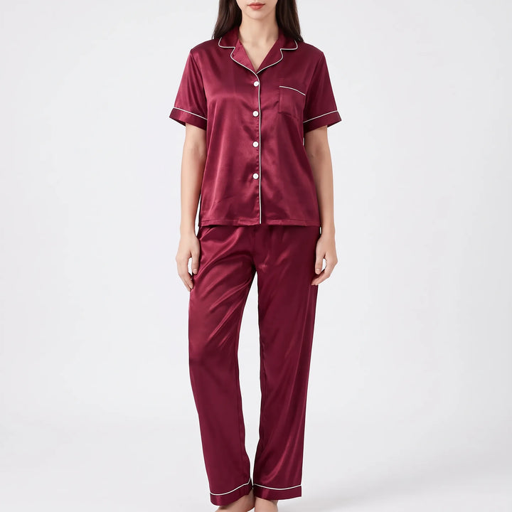 Studio front view of a woman wearing the burgundy satin pajamas with white buttons, piped collar and pocket, and long pants. 6