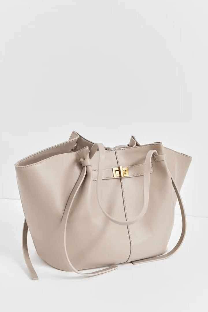 Beige tote detail at a three-quarter angle, showing the gold twist-lock, knotted side ties and long straps.