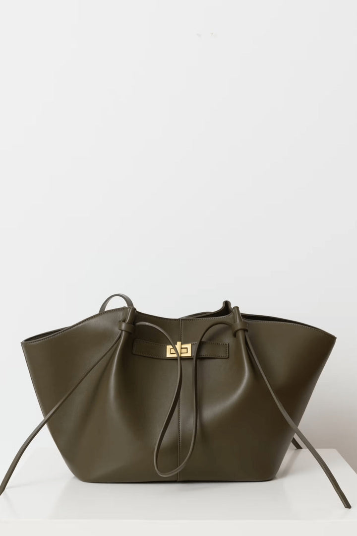 Olive green tote detail with long straps looped forward, gold twist-lock and side ties, displayed on a white surface.