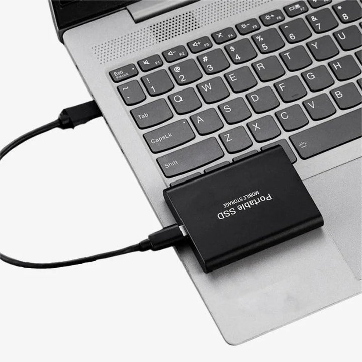 Black slim drive connected by a cable and resting on a silver laptop's keyboard deck.