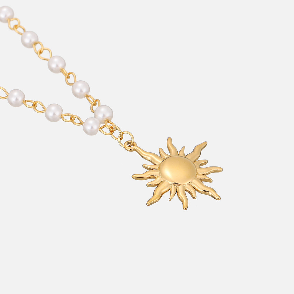 Angled close-up of the gold sun pendant and pearl chain lying on a light surface 2