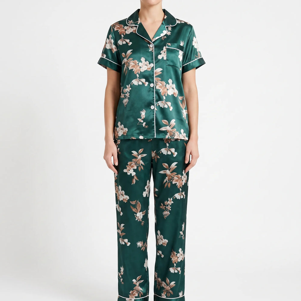 Front view of a model standing against a plain white backdrop, wearing the short-sleeve satin top with chest pocket and matching floral trousers. 2