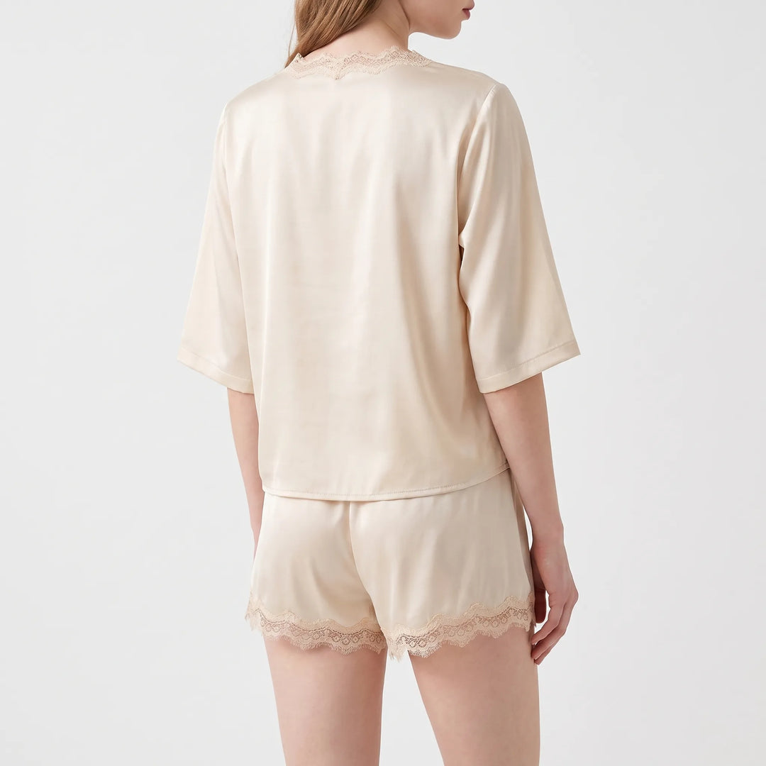 Back view of the cream satin pajama set on a model, showing the plain back and lace hems on the shorts. 3