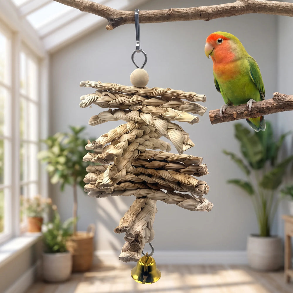 Braided straw toy with a bell hanging from a branch in a bright room, with a green and orange lovebird perched beside it. 2