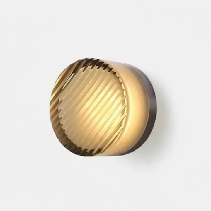 Wall lamp with diagonal ribbed amber-toned glass and a dark metal backplate, glowing softly on a light background. 35