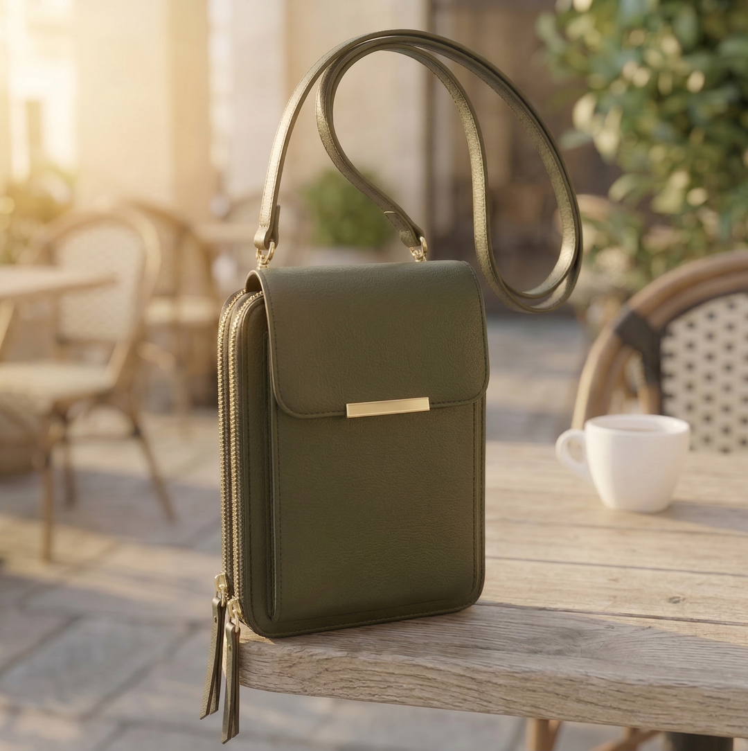 Olive green crossbody bag with gold clasp and zipper pulls on a weathered outdoor table.