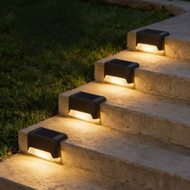 Black solar step lights shining warm light on rough stone steps beside a dark lawn.