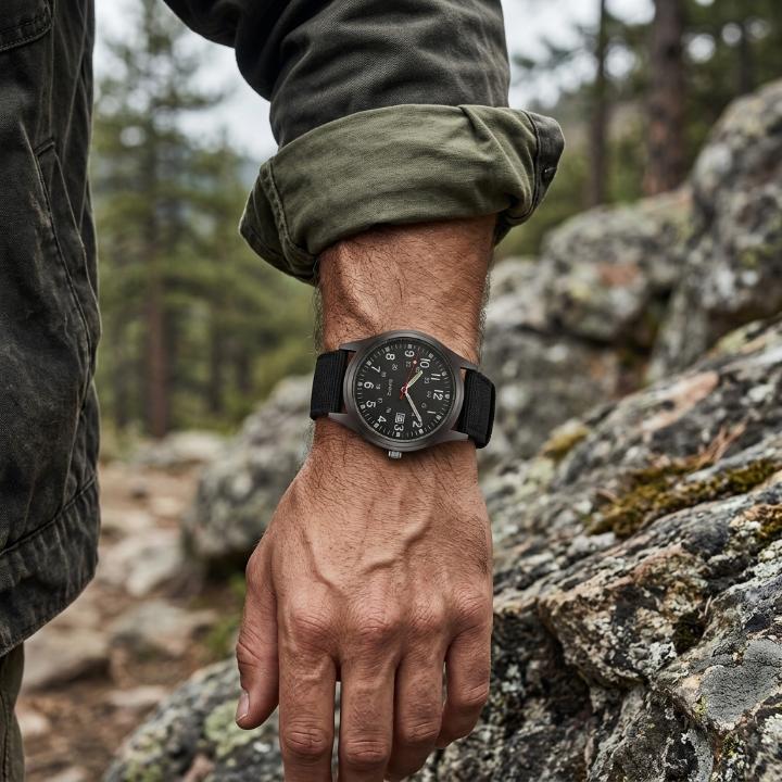 Black military watch with nylon strap, another view while worn on a rolled-up sleeve outdoors.