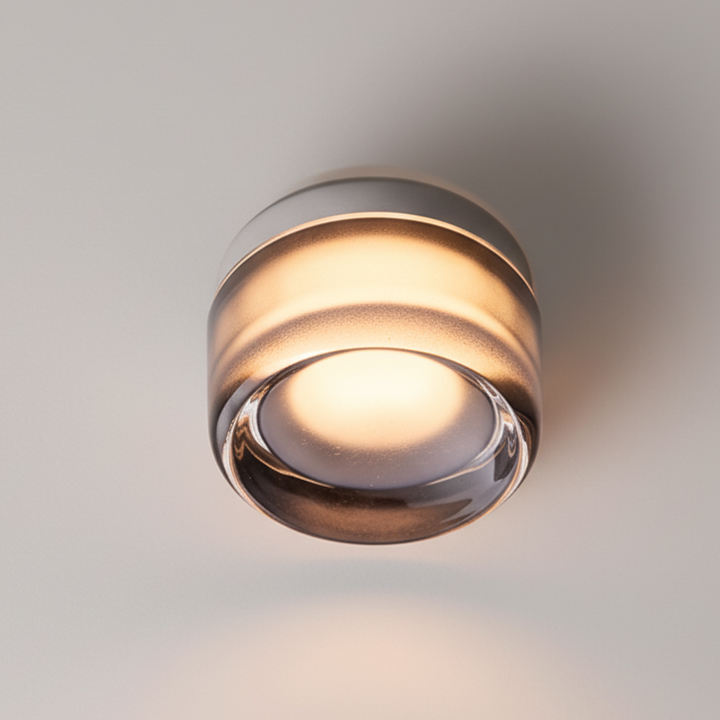 Small round lamp mounted on a ceiling, giving off a warm glow through its smoky clear glass lower edge. 26